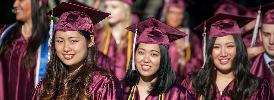 Three graduating students smiling in cap and gown