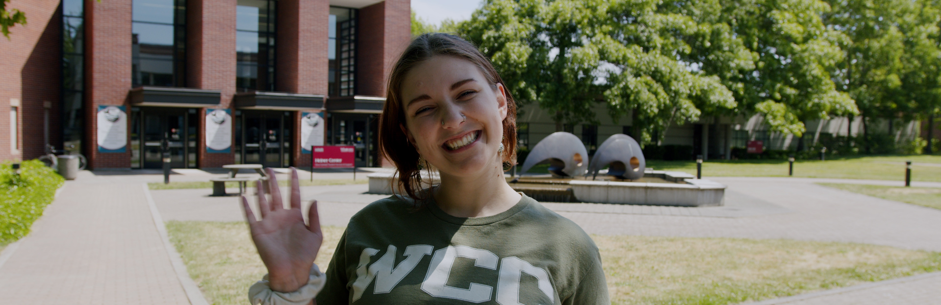 An image of Megan, a pod leader, smiling and waving in front of Orca Central
