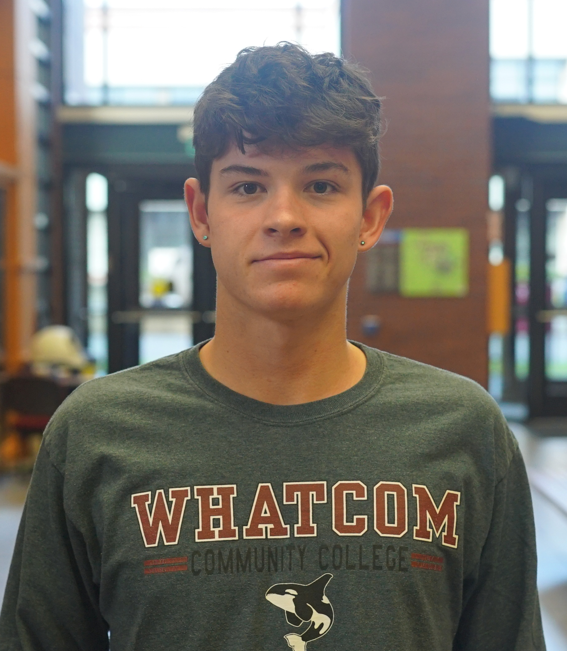 Jacob standing in the Heiner Foyer wearing a Whatcom Community College shirt with an Orca